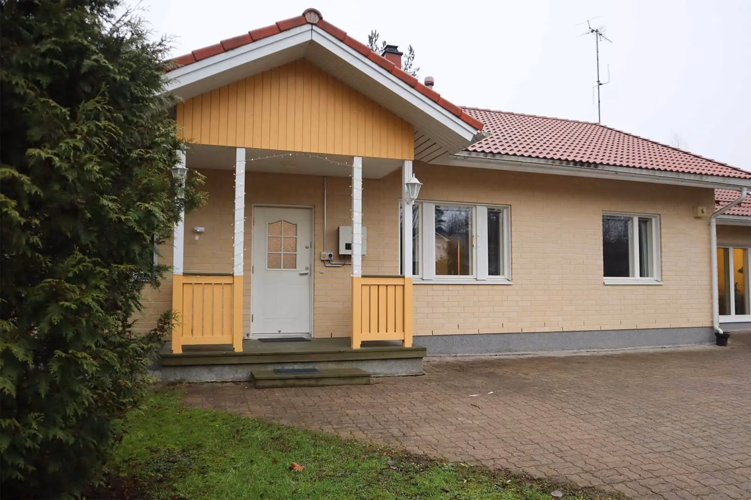 Keltainen omakotitalo ulkoa kuvattuna. Vuonna 2003 rakennettu tiilitalo punaisella katolla.