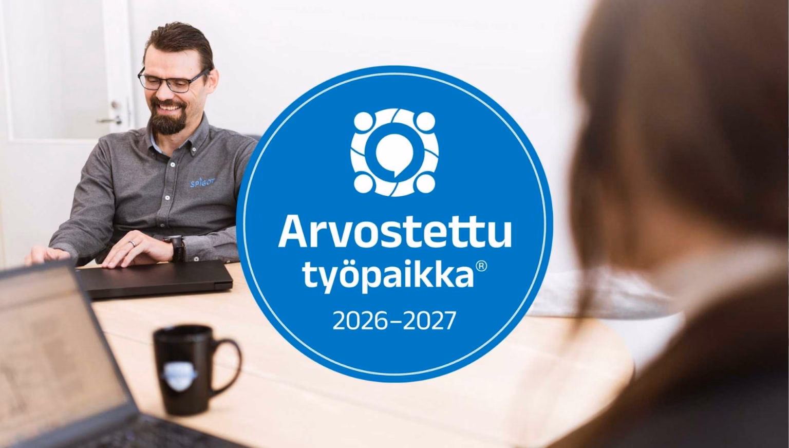 Arvostettu työpaikka® -sertifikaattilogo 2026–2027, joka taustalla Spigotin hymyilevä työntekijä.